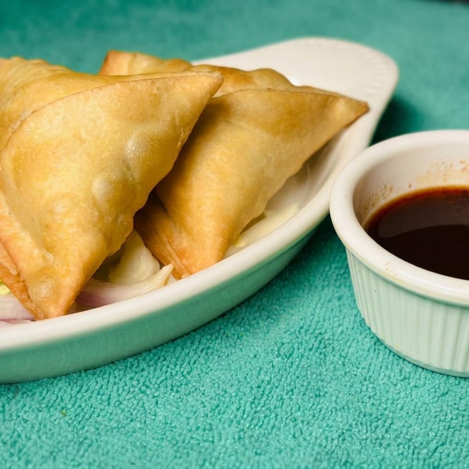 Golden fried triangular pastries served with sliced onions and a small bowl of dark dipping sauce.