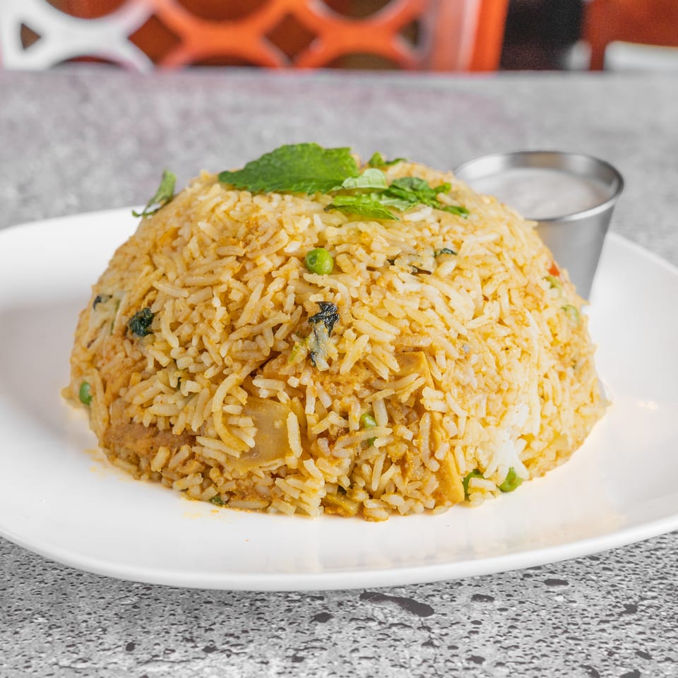 Spiced vegetable rice topped with fresh mint, served on a white plate with a small bowl of sauce.