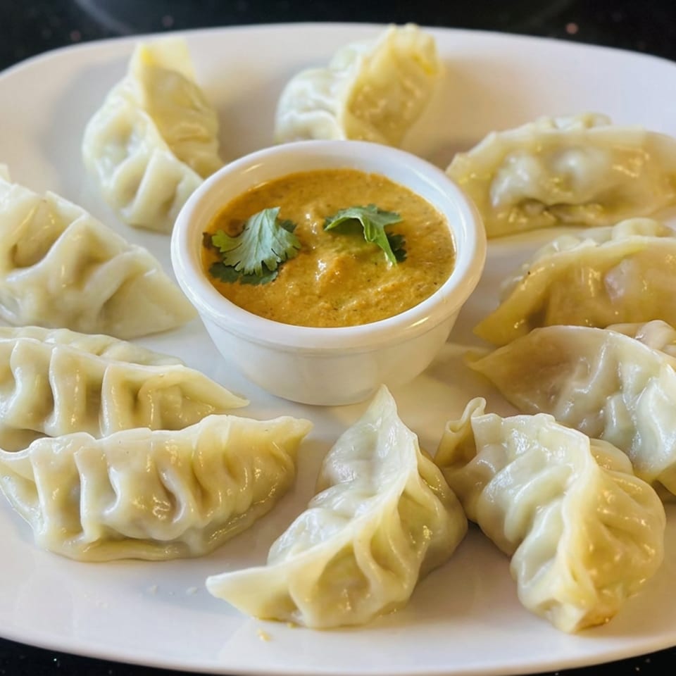 Steamed dumplings arranged around a bowl of golden dipping sauce garnished with cilantro on a white plate.