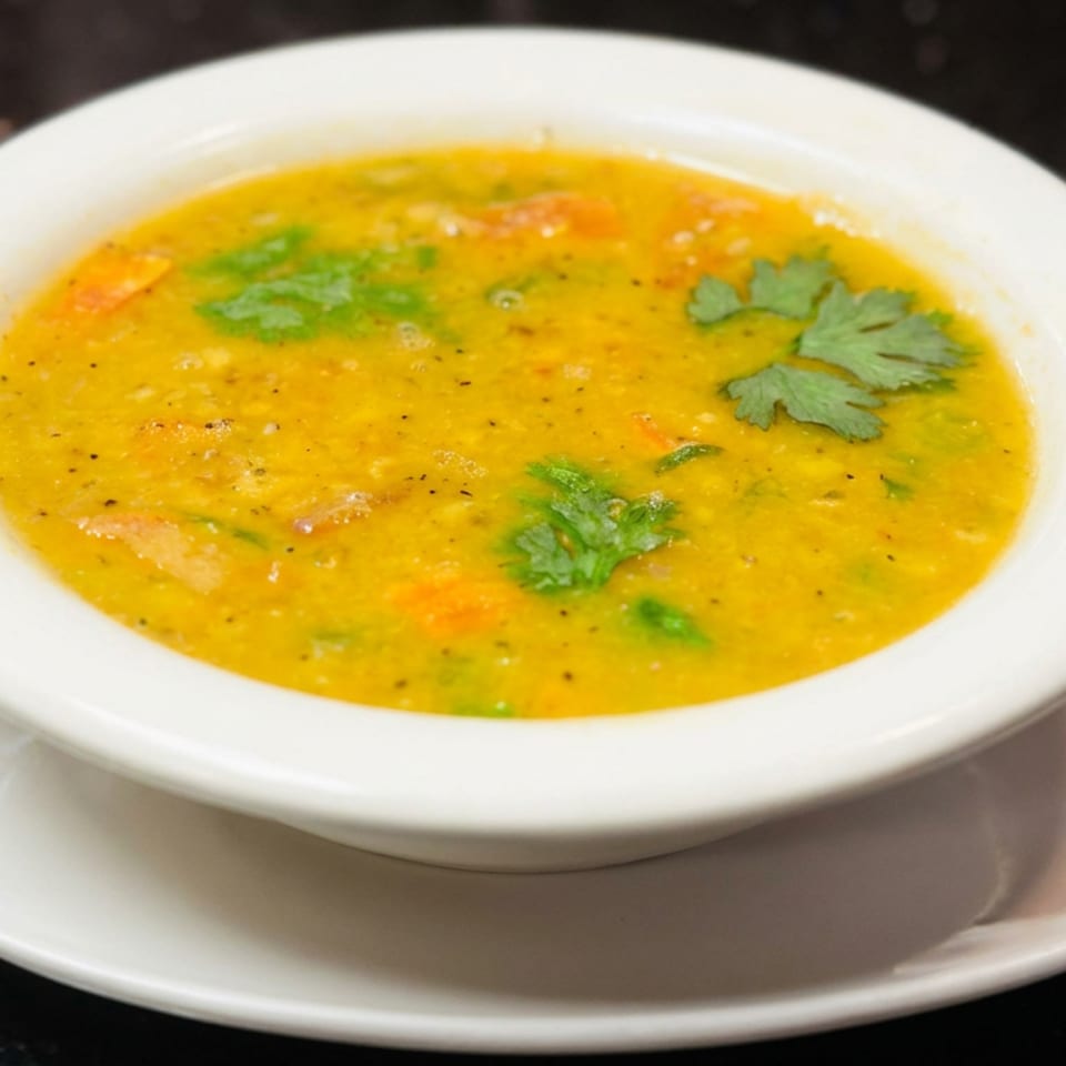 Bowl of creamy golden vegetable soup garnished with fresh cilantro on a white saucer atop a dark countertop.