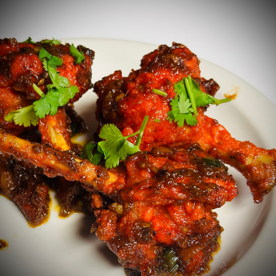 Close-up of spicy red glazed chicken wings garnished with fresh cilantro on a white plate.