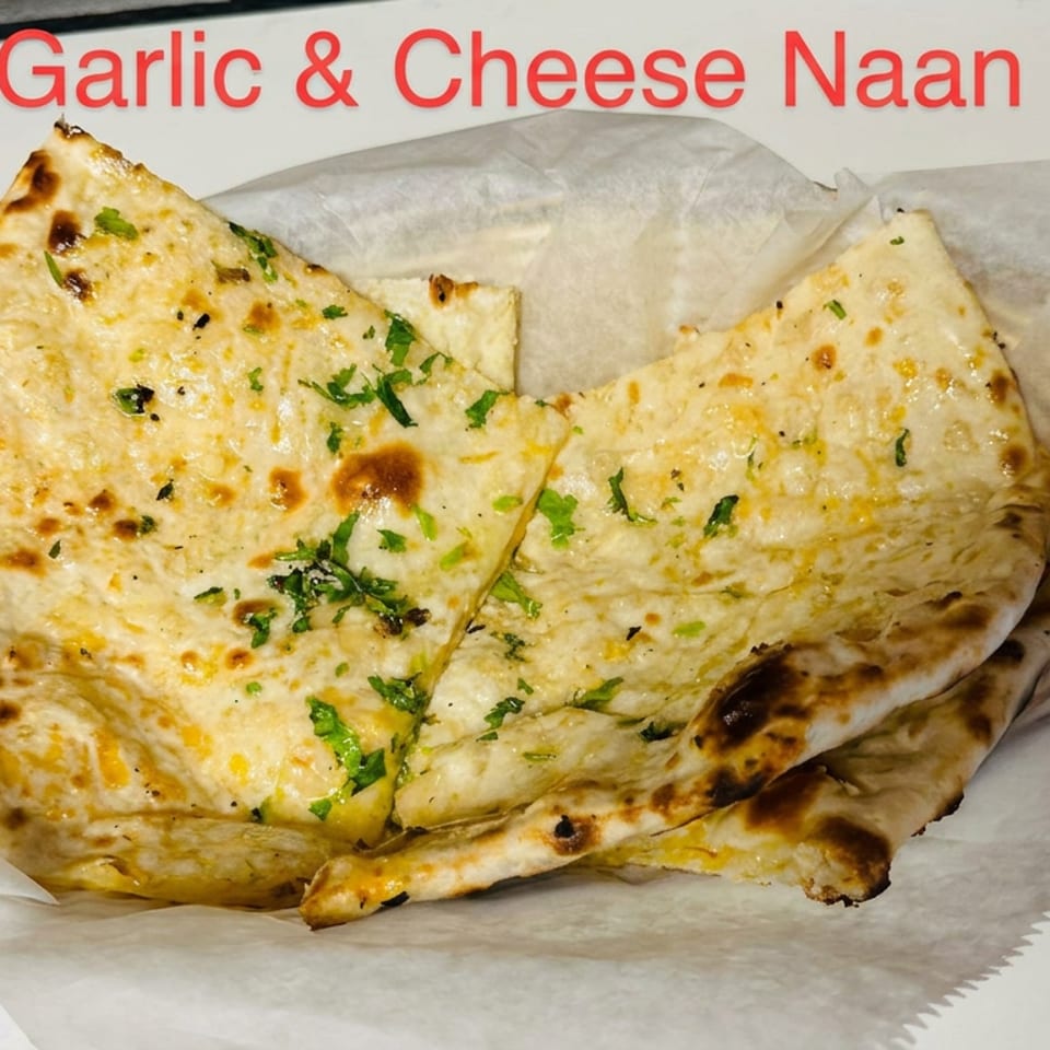 Stack of golden garlic and cheese naan breads garnished with chopped cilantro on parchment paper.